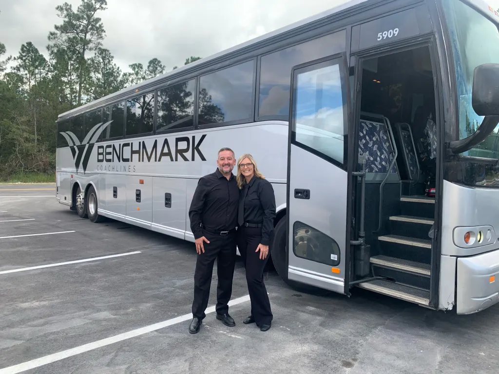 The Benchmark Coachlines team beside a luxury motorcoach with the boarding door open in North Florida